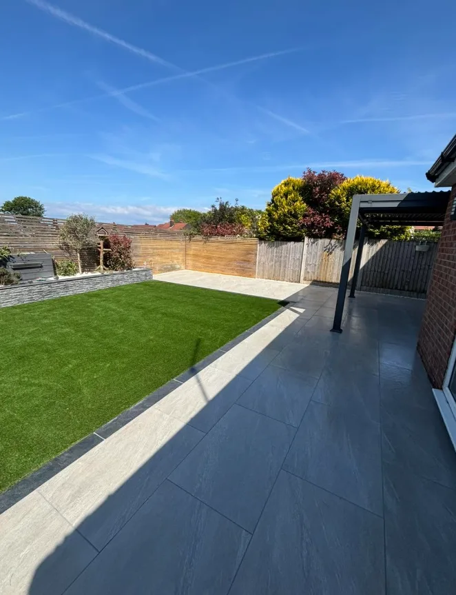 Wide sunny garden with patio, lawn, stone wall and pergola