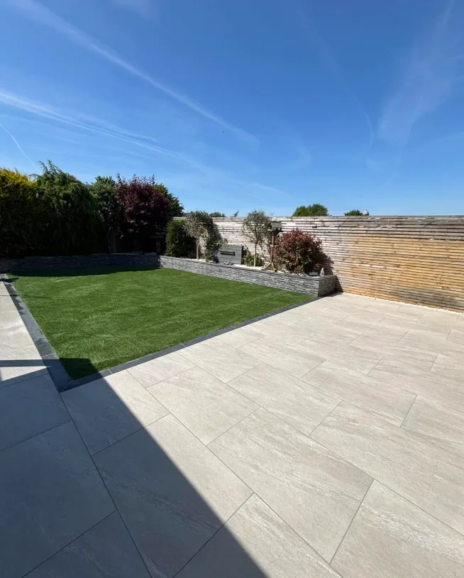 Sunny porcelain patio, lawn and stone retaining wall garden