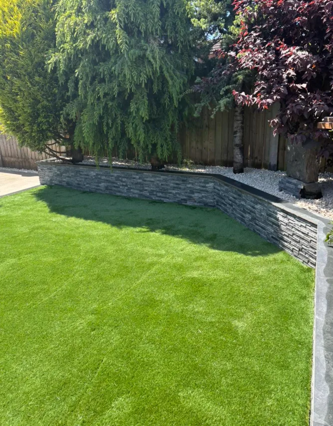 Close-up of artificial lawn against a dark stone retaining wall