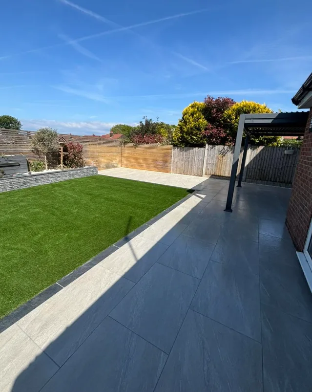 Garden corner with lawn, stone wall and pergola in sunshine