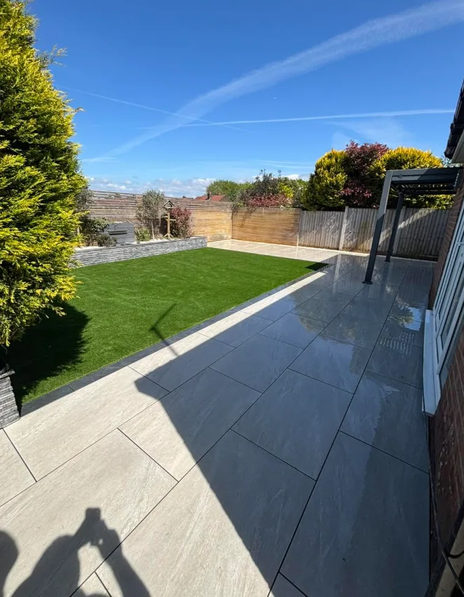 Wide angle sunny patio and lawn with stone wall and pergola