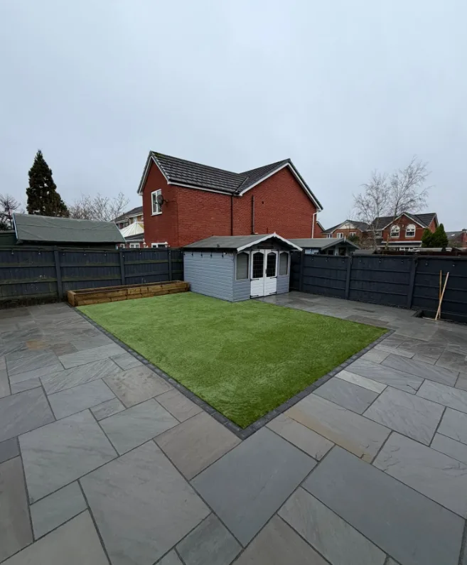 Grey stone patio with square lawn, shed and dark fencing