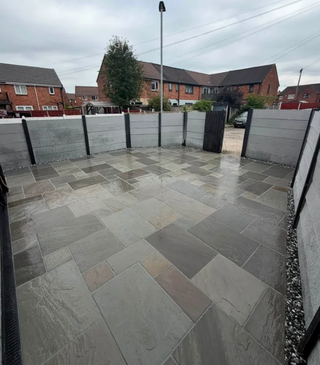 Mixed-tone stone patio enclosed by grey fence panels