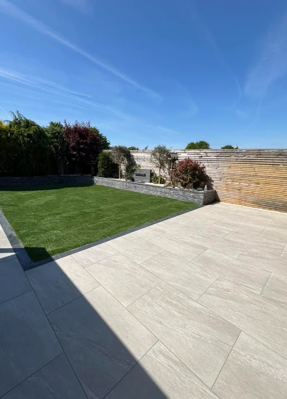 Sunny porcelain patio, lawn and stone retaining wall garden by KLG Landscape